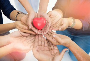 Photo of hands clasping together, holding up a love heart